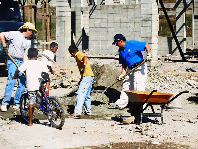 Two men and three boys work at a construction site shoveling dirt.