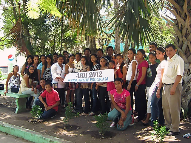 A large group of students stand under palm trees and hold a banner that reads 'AHH 2012 Scholarship Program'