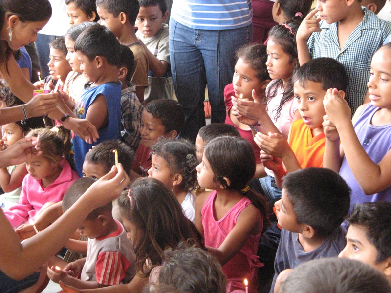 Students stand and sit together in a group as adults hand out celebratory candles.