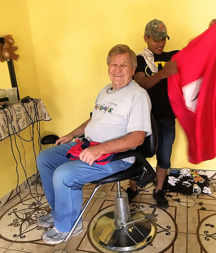 A member of AHH smiles and sits in a barber chair while a hairdresser prepares to cut his hair.