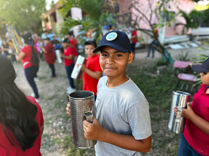 A close up of a boy holding a stainless steel metal guiro (percussion instrument) outside with a large group of band students.