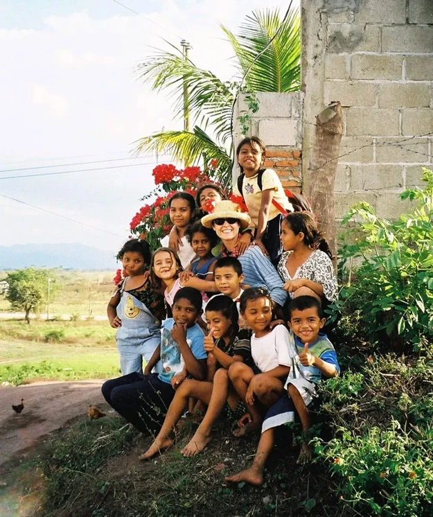 A group of smiling young children gather around an AHH volunteer alongside rural road in Honduras.